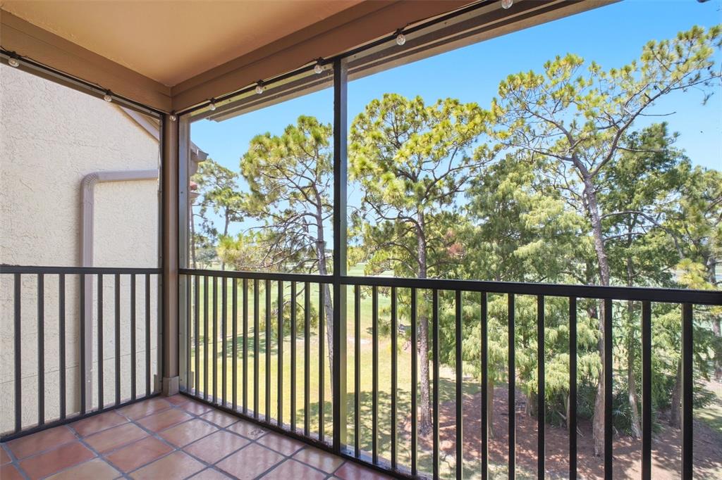 A screened-in balcony with tile flooring overlooks a golf course and pine trees — 2400 FEATHER SOUND DRIVE UNIT 236, CLEARWATER, FL