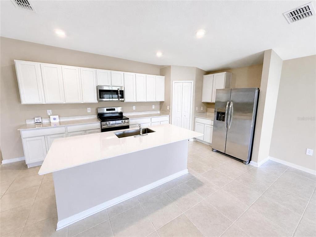 A kitchen features white cabinets, stainless steel appliances, a center island, and light tile flooring — 2862 PENNACHIO DRIVE, LAKE WALES, FL