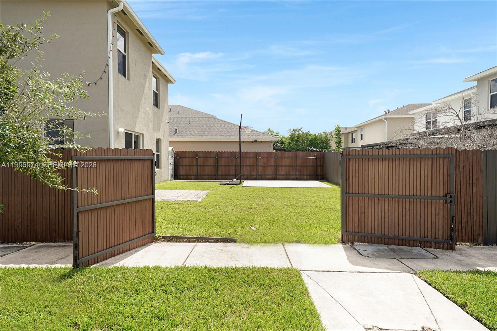 A fenced backyard features a grassy lawn, a concrete patio, and a basketball hoop — 572 NE 6th Pl, Homestead FL 33034, HOMESTEAD, FL