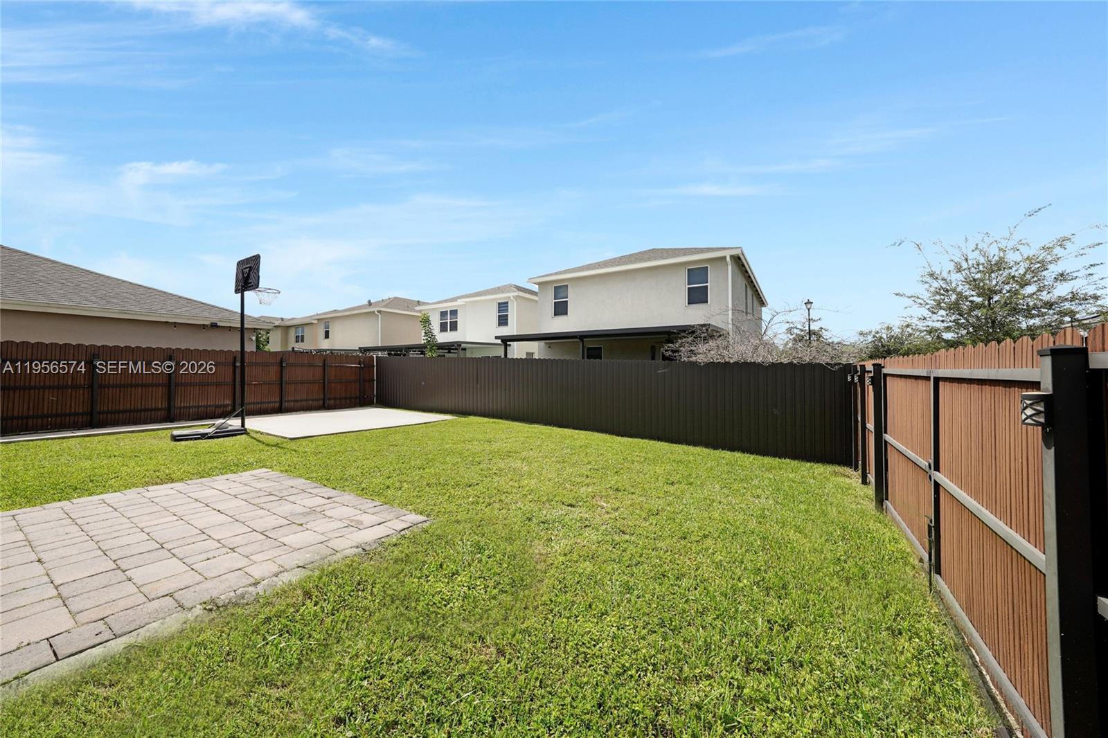 A fenced backyard features a grass lawn, a paved patio, and a basketball hoop — 572 NE 6th Pl, Homestead FL 33034, HOMESTEAD, FL