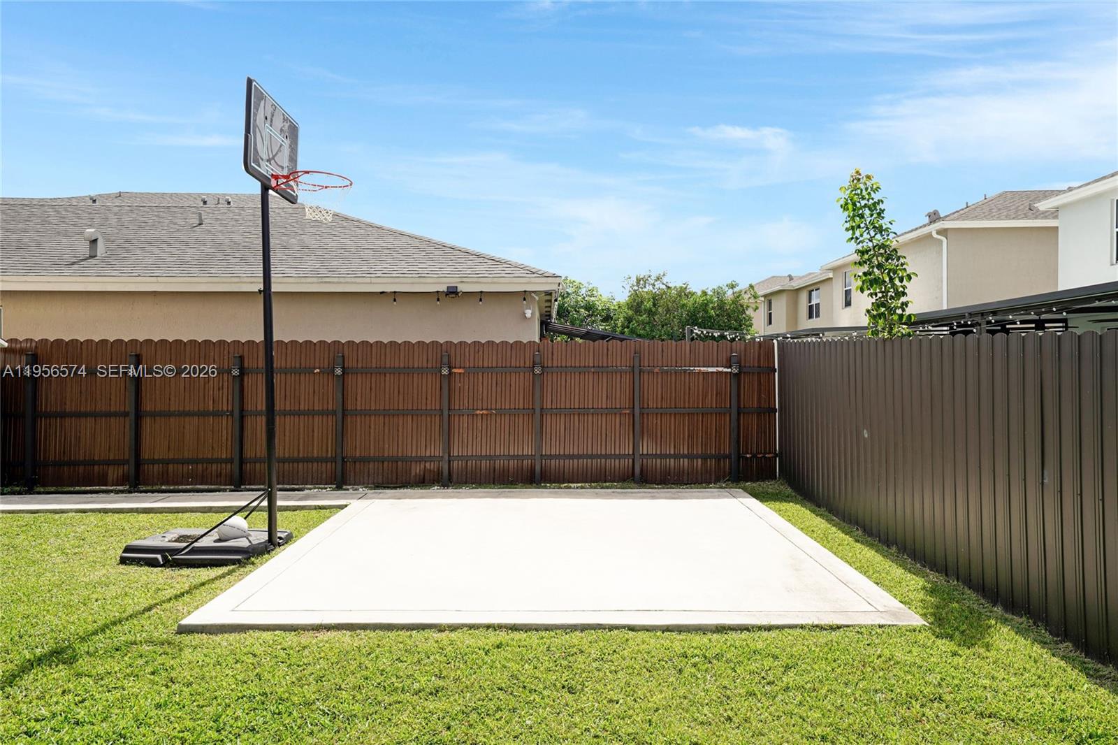 A backyard features a concrete basketball court with a hoop and a wooden fence — 572 NE 6th Pl, Homestead FL 33034, HOMESTEAD, FL