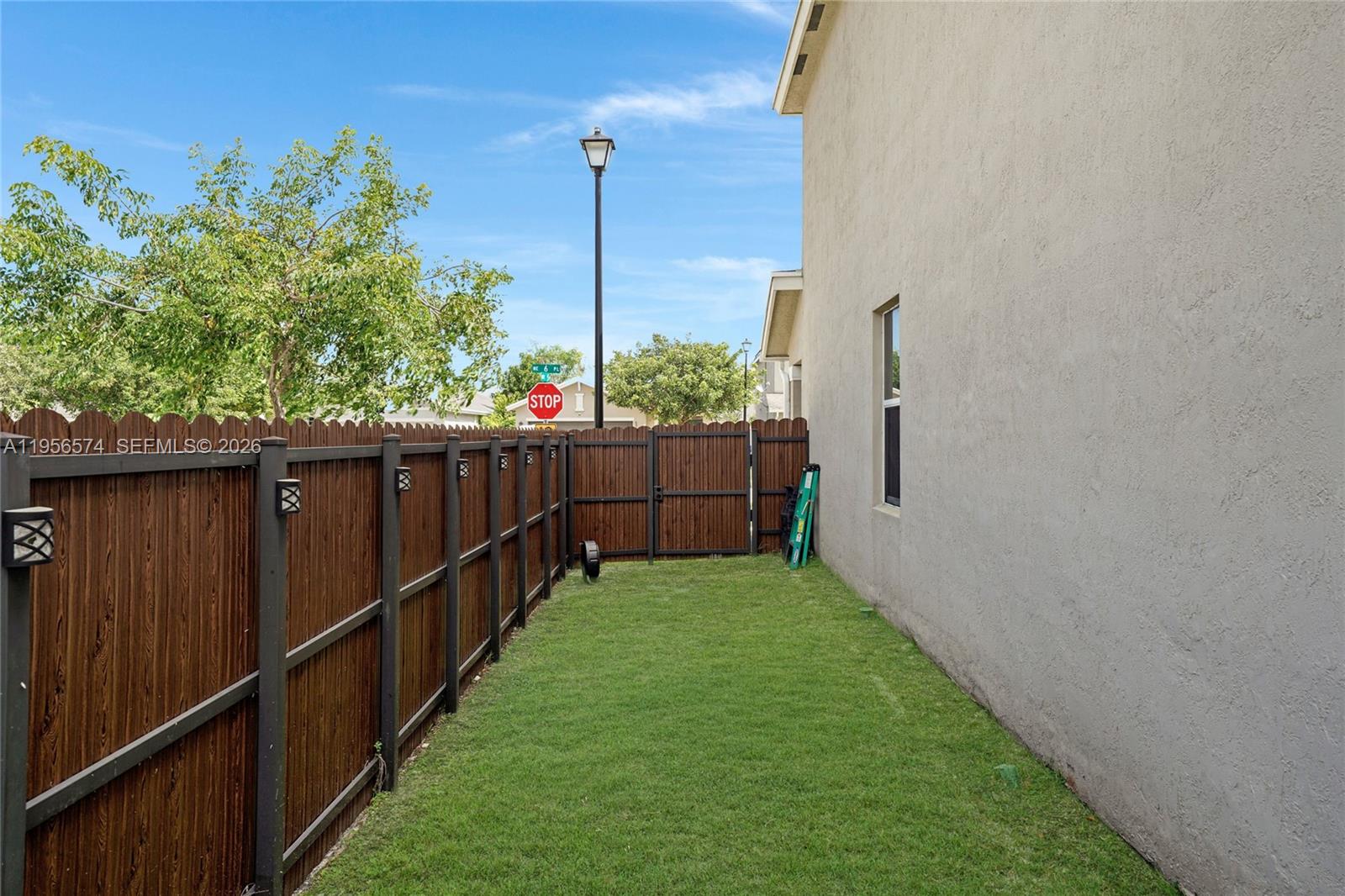 A narrow grassy side yard is enclosed by a tall wooden fence next to a house — 572 NE 6th Pl, Homestead FL 33034, HOMESTEAD, FL