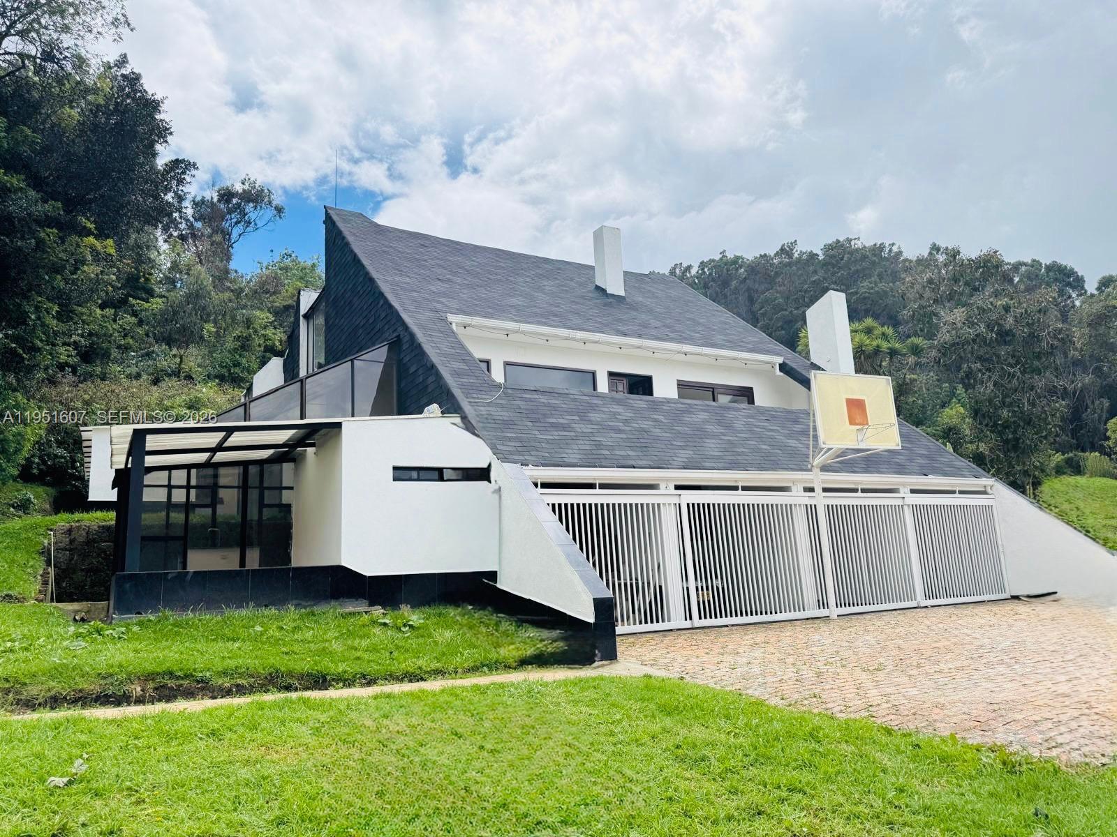 A modern house with a sloped roof, white walls, and a gated garage area — Floresta de la Sabana Floresta de la Sabana, FL