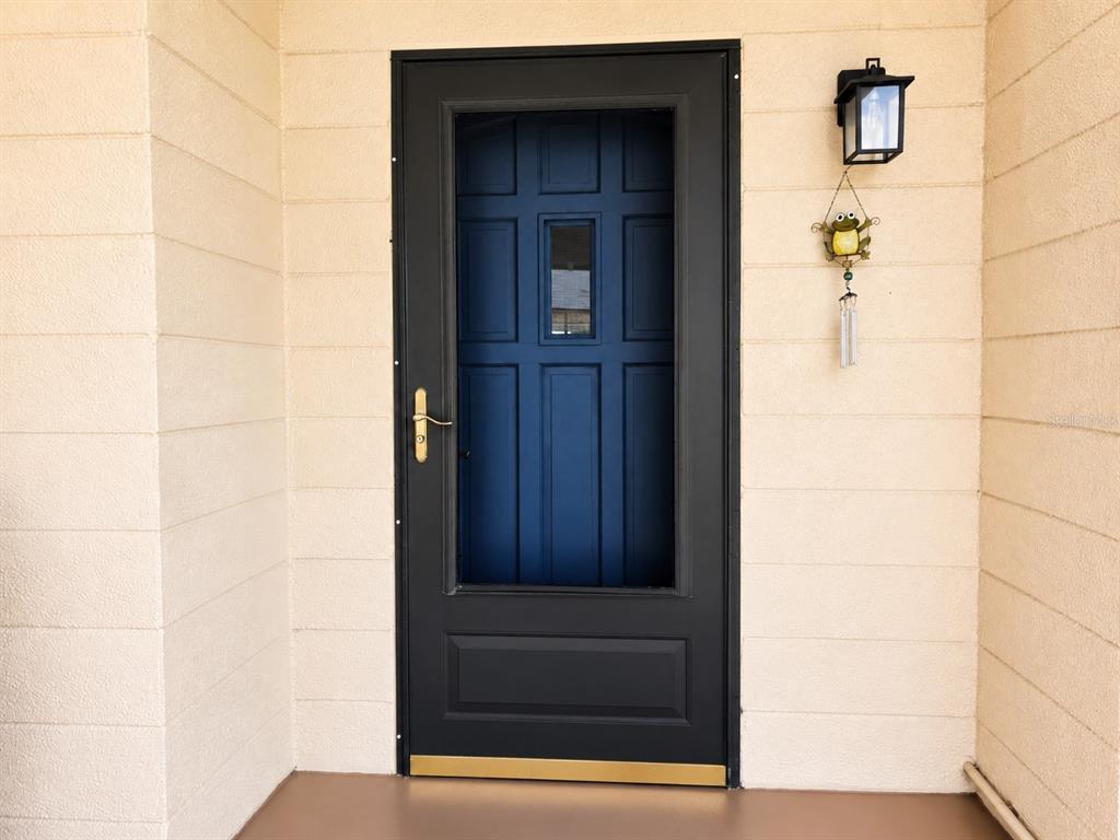 A covered patio with two wicker chairs leads to a dark blue front door — 617 PARK CIRCLE UNIT 26, BRADENTON, FL