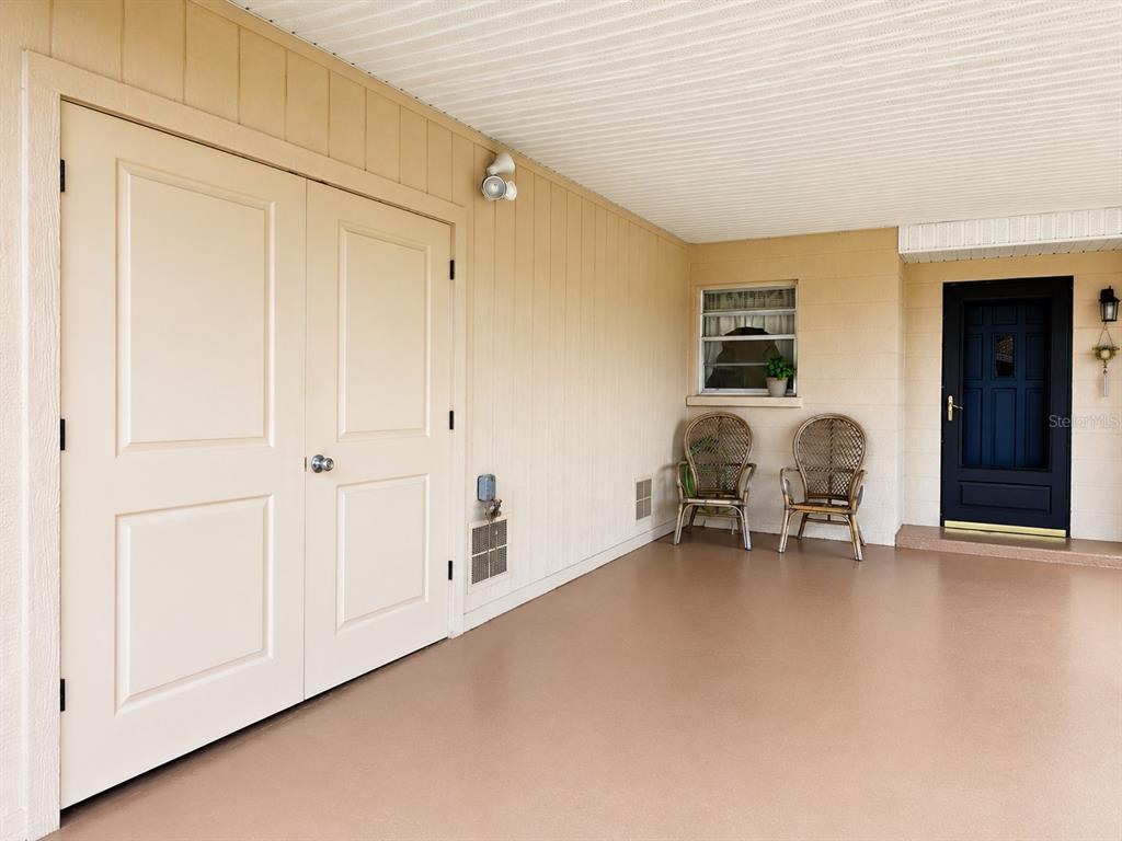 Two wicker chairs sit on a covered porch next to a window with a potted plant — 617 PARK CIRCLE UNIT 26, BRADENTON, FL