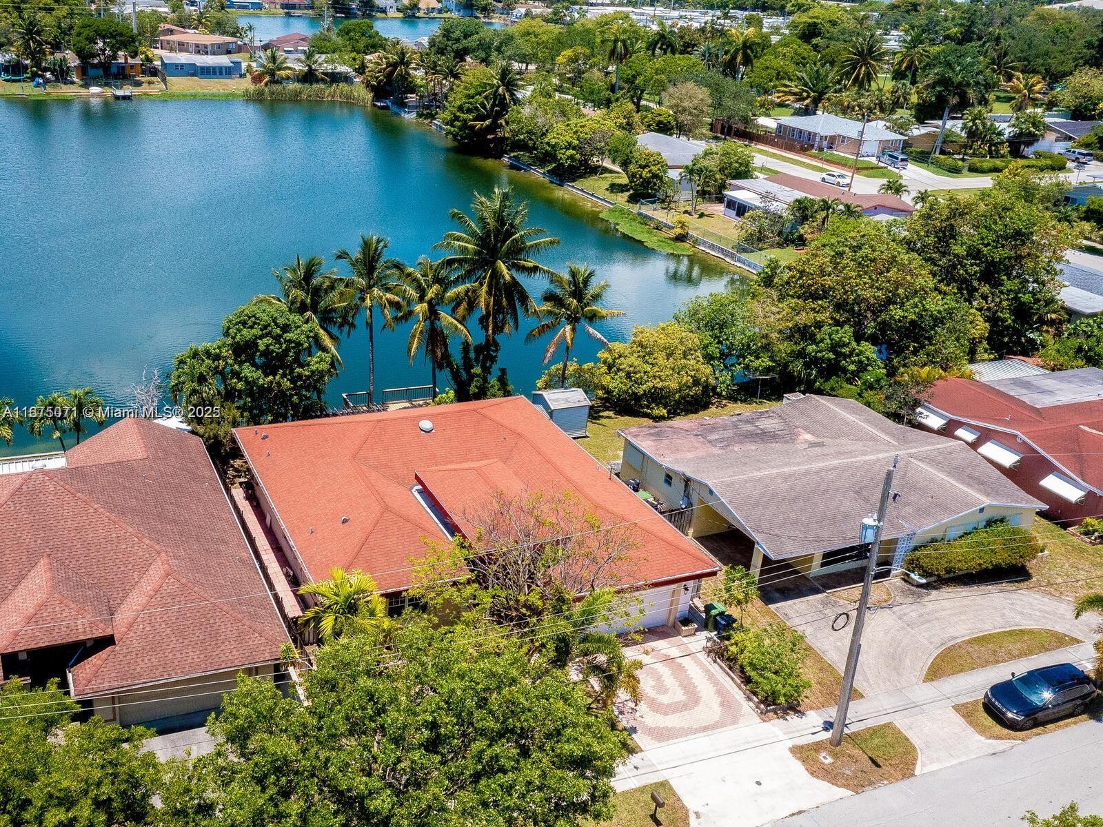An aerial view shows a house with a red roof situated next to a lake — 232 SW 7th Ave, Hallandale Beach FL 33009, HALLANDALE BEACH, FL