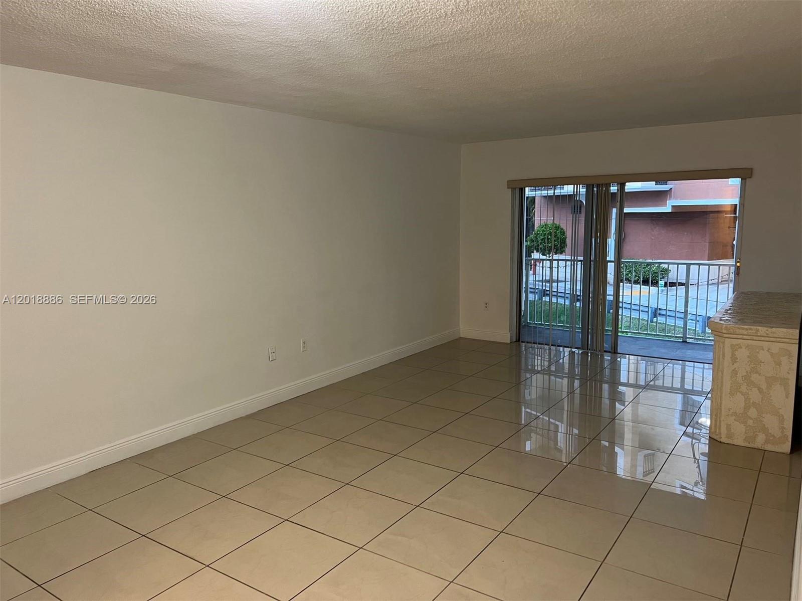 An empty living room features beige tile flooring, white walls, and a sliding glass door — 7324 SW 82nd St # B210, Miami FL 33143, MIAMI, FL
