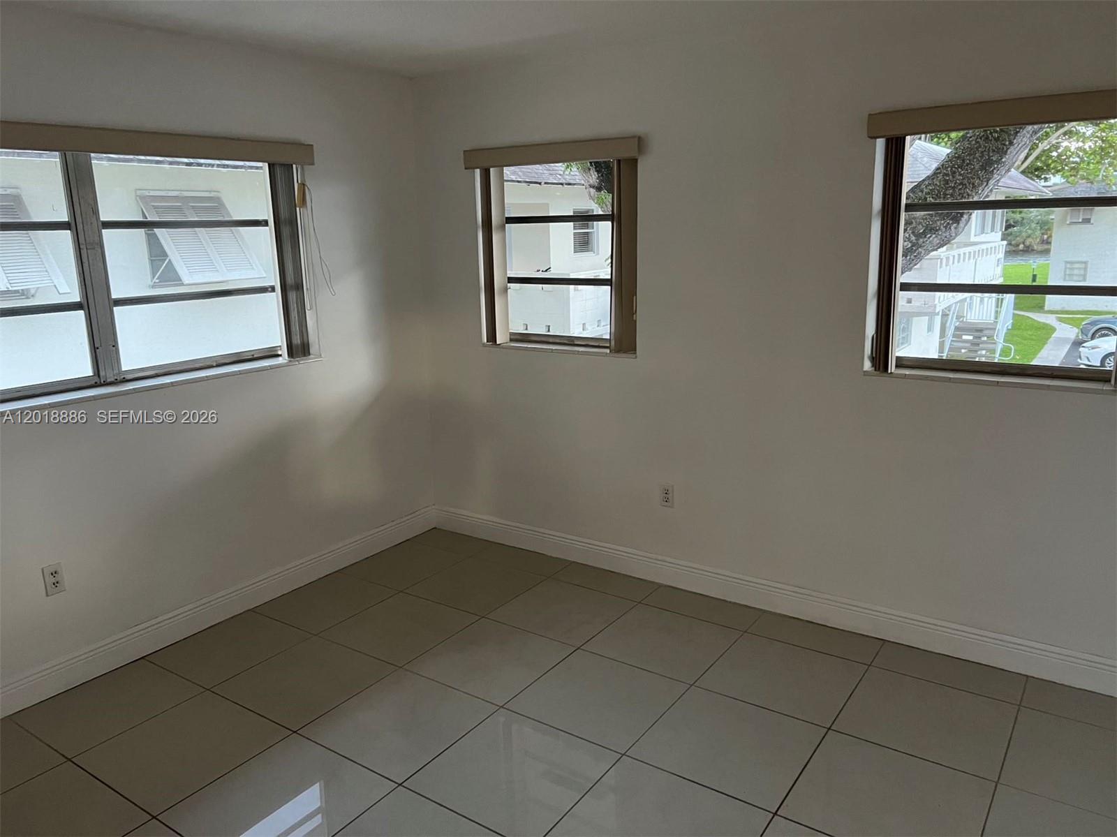 An empty room features white walls, light-colored tile flooring, and three windows — 7324 SW 82nd St # B210, Miami FL 33143, MIAMI, FL