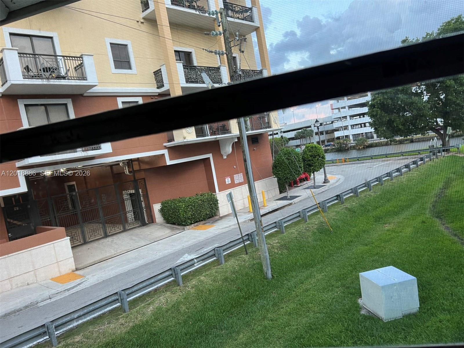 A view from a window shows a multi-story building, a road, and a grassy area — 7324 SW 82nd St # B210, Miami FL 33143, MIAMI, FL