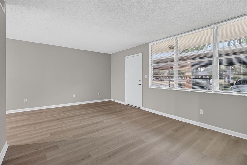 An empty living room features light gray walls, wood-look flooring, and a large window — 4885 1ST STREET NE UNIT 109, ST PETERSBURG, FL