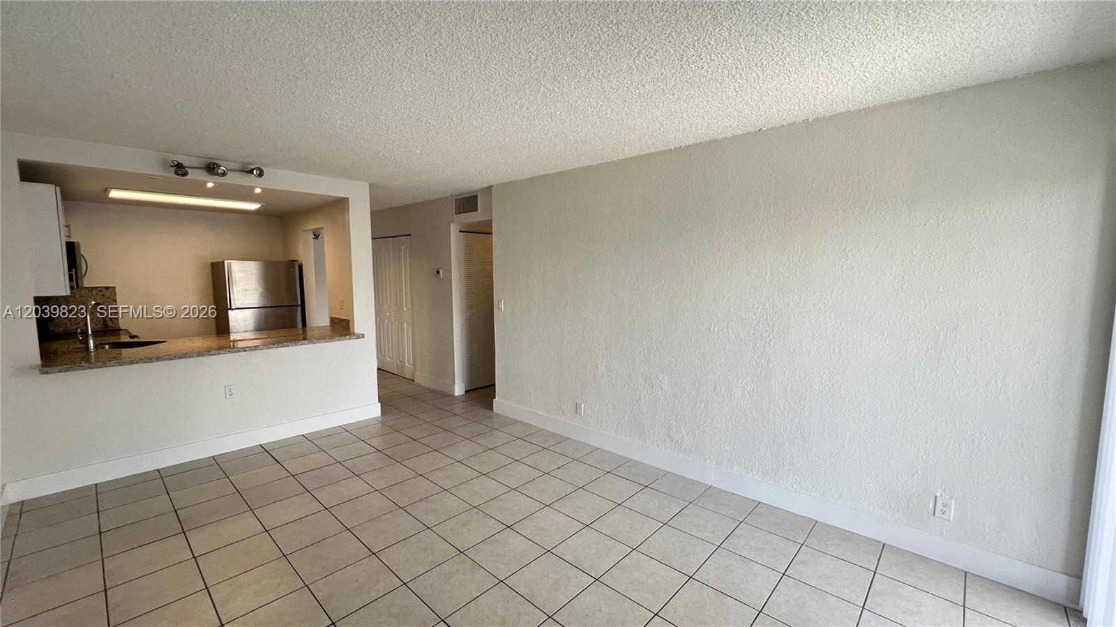 An open-concept living area features light-colored tile flooring, a textured ceiling, and a kitchen pass-through — 4550 NW 9th St # 817E, Miami FL 33126, MIAMI, FL