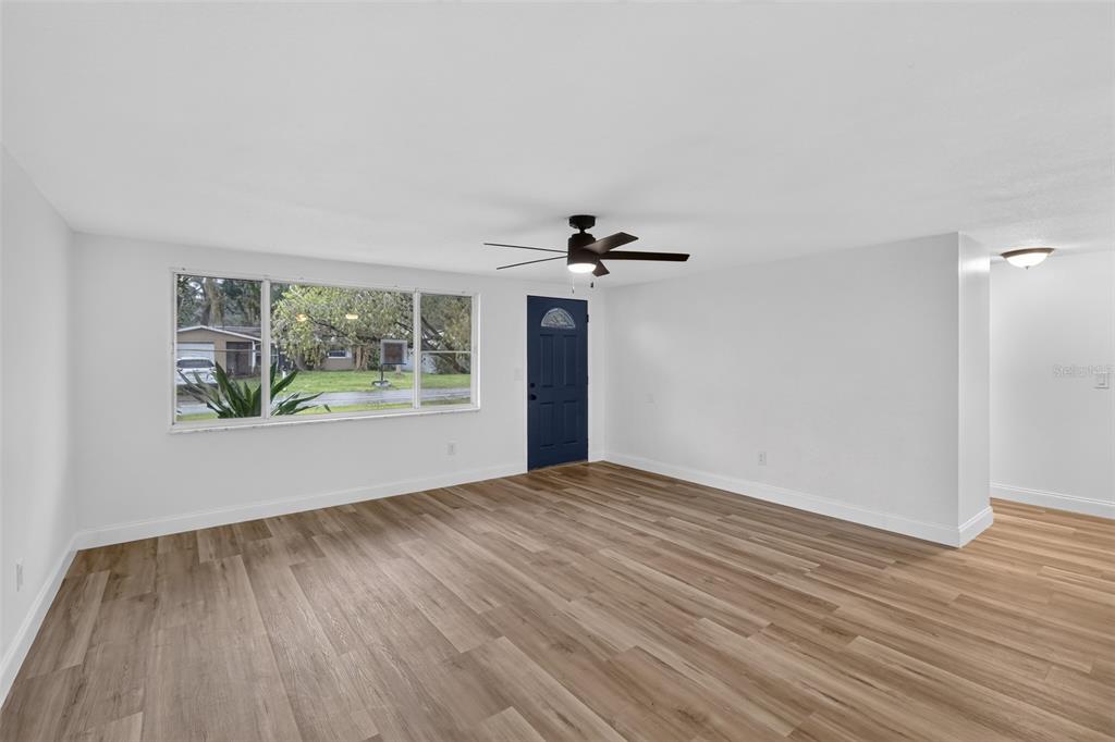 A bright living room with light wood-look flooring, a ceiling fan, and a blue door — 5644 BERLIN DRIVE, PORT RICHEY, FL