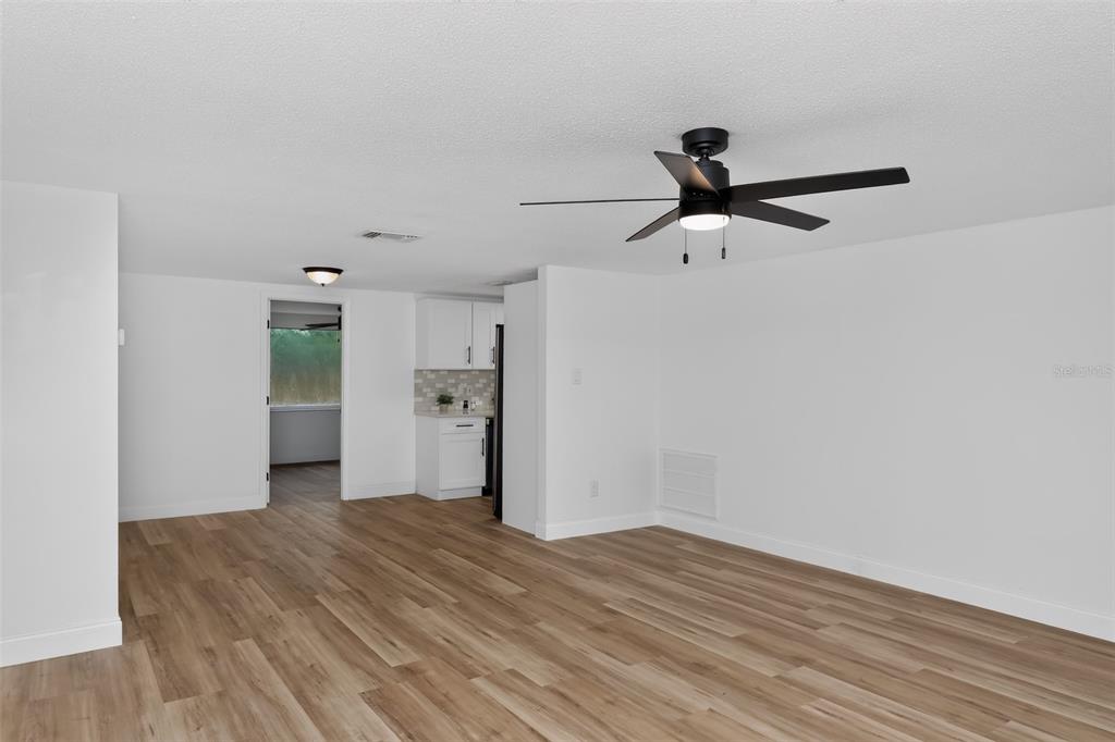 A bright, open-concept living area features light wood-look flooring, white walls, and a ceiling fan — 5644 BERLIN DRIVE, PORT RICHEY, FL