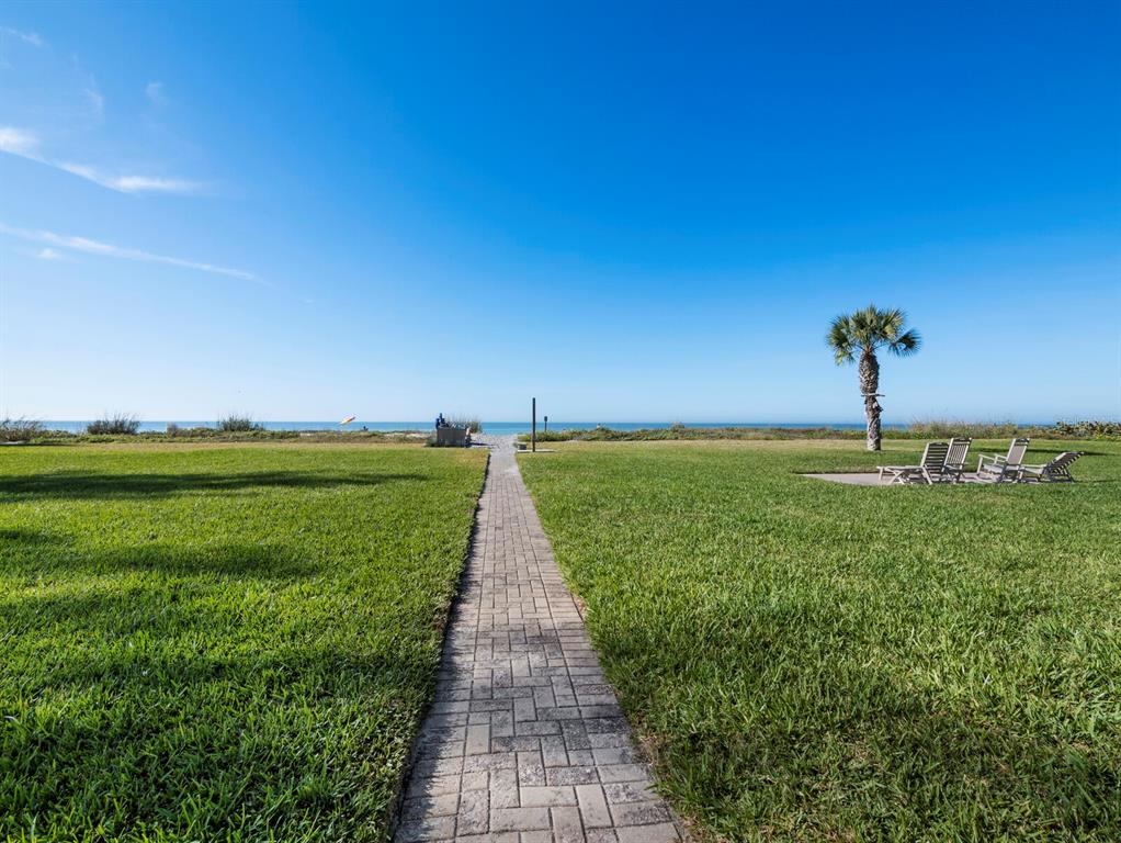 A brick walkway leads through a grassy lawn toward the ocean under a clear sky — 5231 GULF OF MEXICO DRIVE UNIT 104, LONGBOAT KEY, FL
