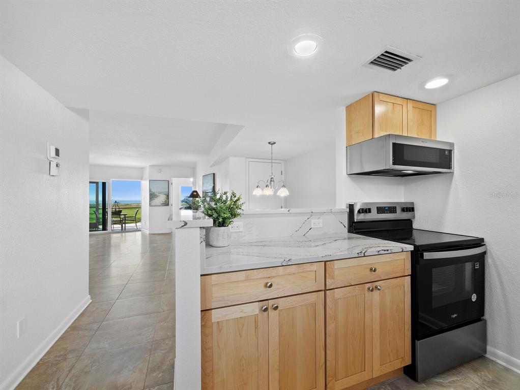 A kitchen with light wood cabinets and marble-look countertops opens to a bright living area — 5231 GULF OF MEXICO DRIVE UNIT 104, LONGBOAT KEY, FL