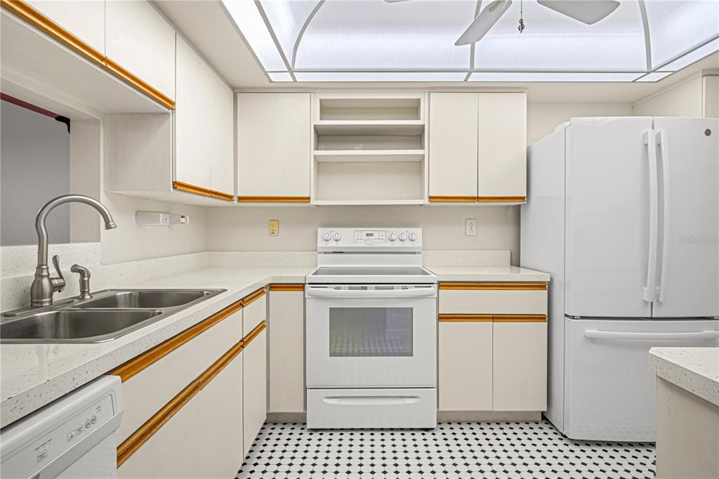 A kitchen features white cabinets with wood trim, white appliances, and a black-and-white tiled floor — 725 PORT MALABAR BOULEVARD NE UNIT 301, PALM BAY, FL