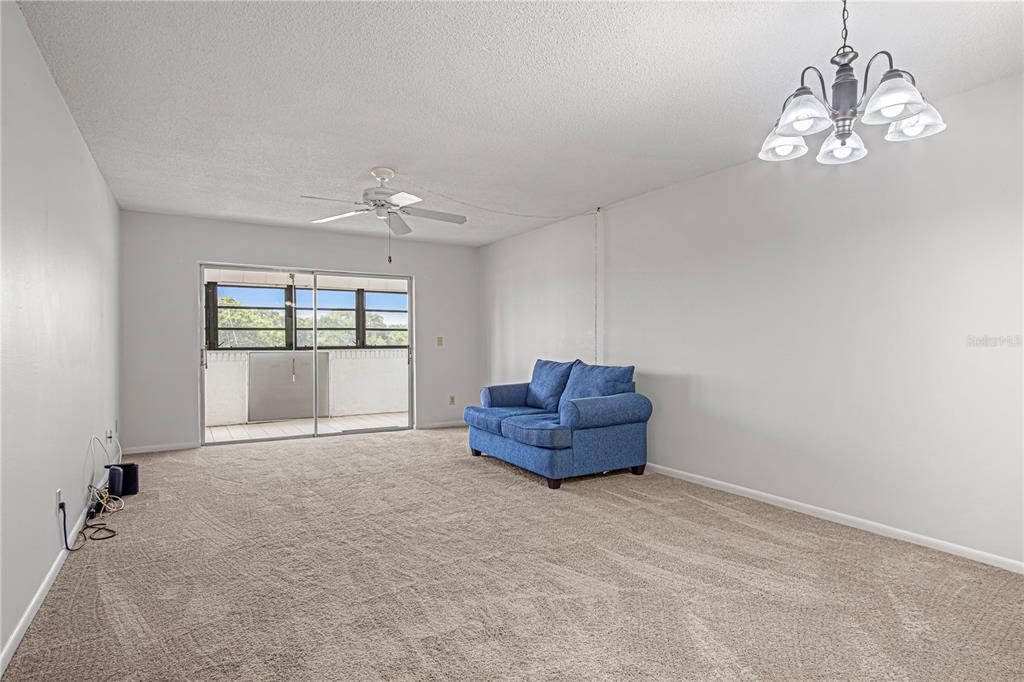A living room with beige carpet, a blue loveseat, a ceiling fan, and a sliding door — 725 PORT MALABAR BOULEVARD NE UNIT 301, PALM BAY, FL