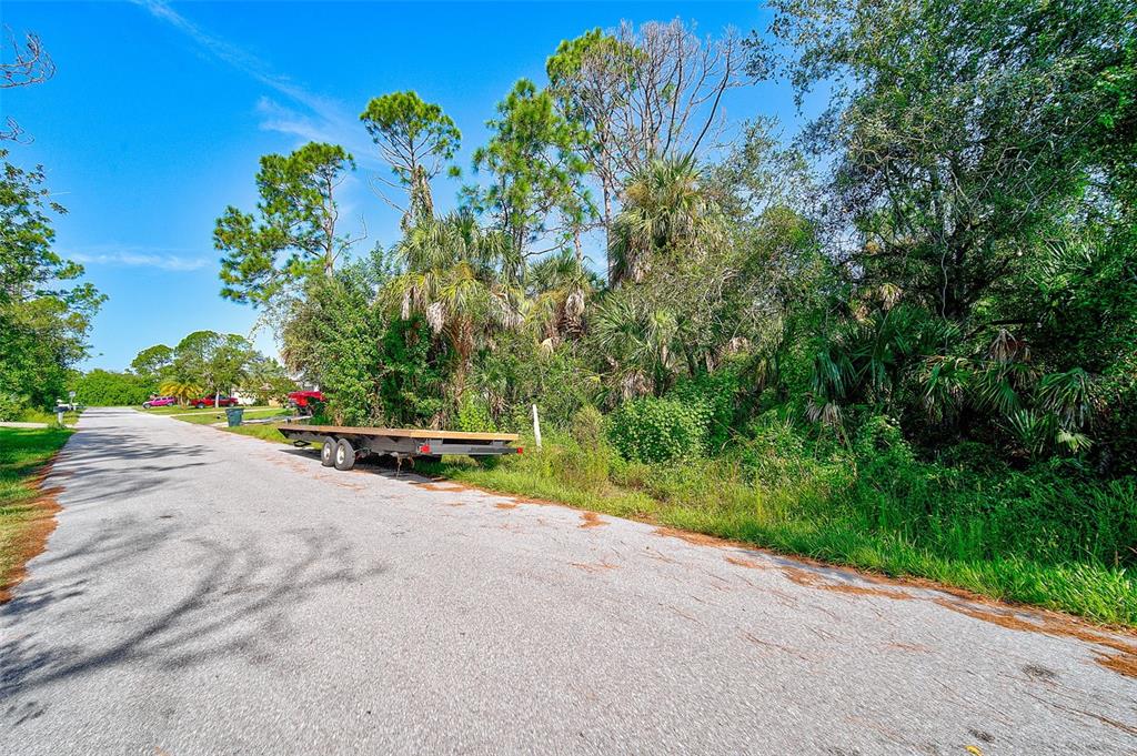 A flatbed trailer sits on the side of a paved road next to dense vegetation — RABBITT AVENUE, NORTH PORT, FL