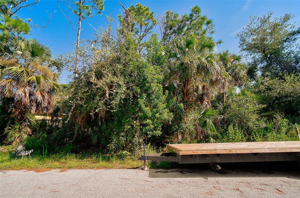 A flatbed trailer sits on a paved road in front of dense trees and palms — RABBITT AVENUE, NORTH PORT, FL