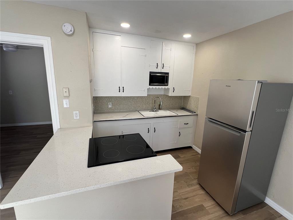 A kitchen features white cabinets, a stainless steel refrigerator, a cooktop, and light countertops — 116 145TH AVENUE E, MADEIRA BEACH, FL