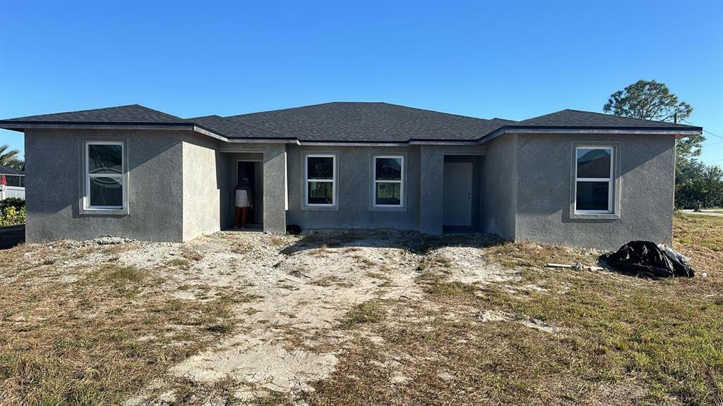 The exterior of a single-story, gray stucco house with a dark shingled roof — 13009 RIDGELY CIRCLE, PORT CHARLOTTE, FL