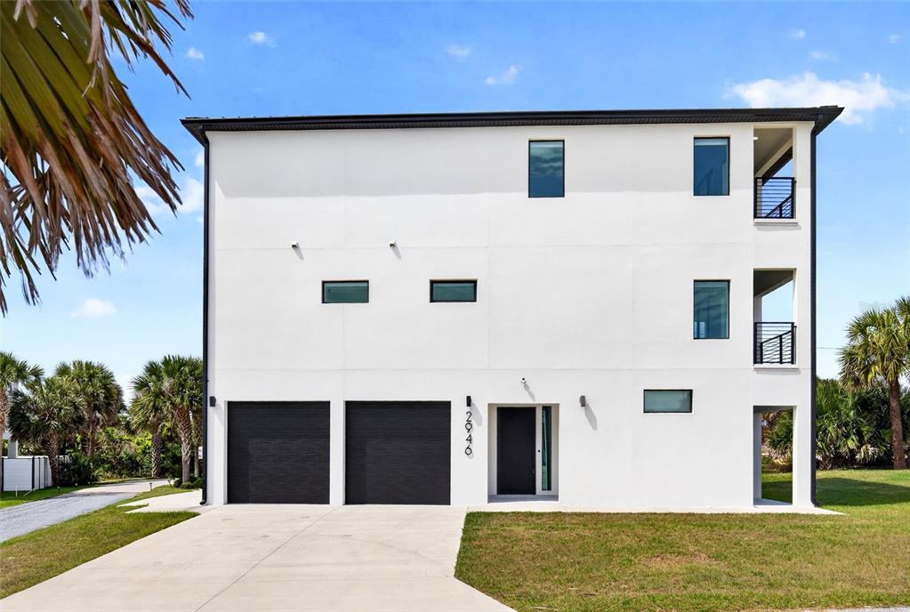 A three-story white modern house features two black garage doors and a front entrance — 2946 N OCEAN SHORE BOULEVARD, FLAGLER BEACH, FL