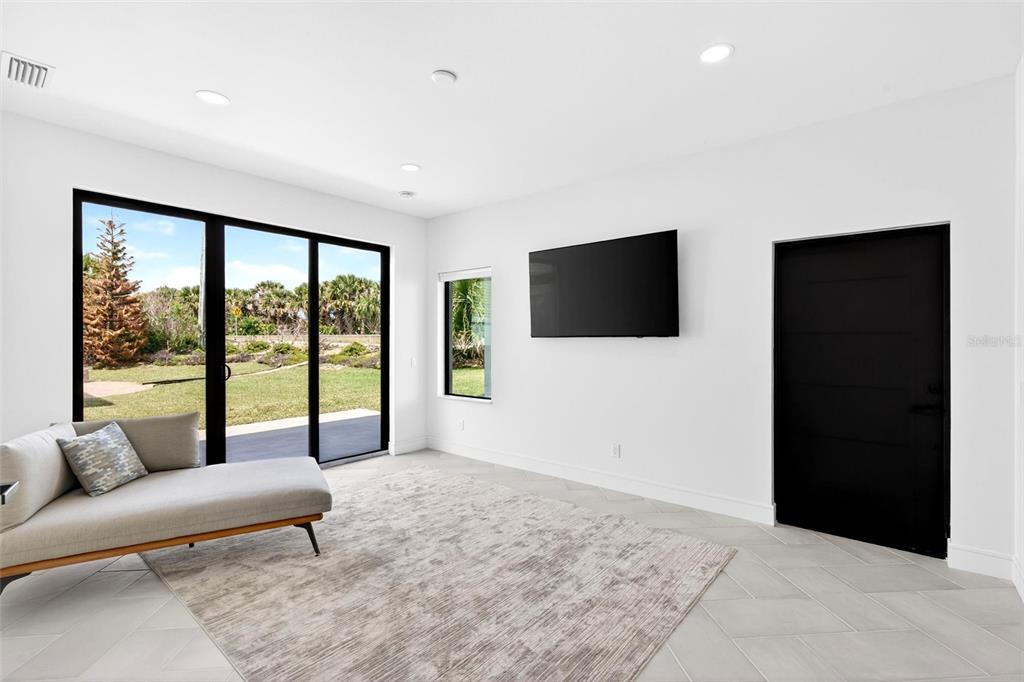 A modern living room features white walls, tile flooring, a gray chaise, and a black door — 2946 N OCEAN SHORE BOULEVARD, FLAGLER BEACH, FL
