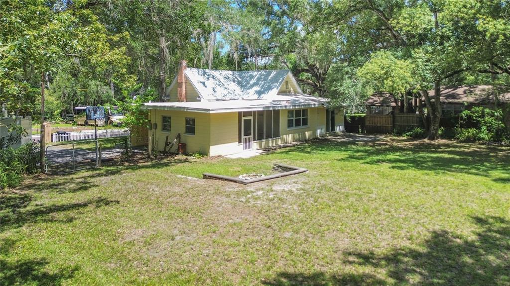 A yellow house with a metal roof and a backyard fire pit sits among trees — 236 PRYOR STREET, BROOKSVILLE, FL