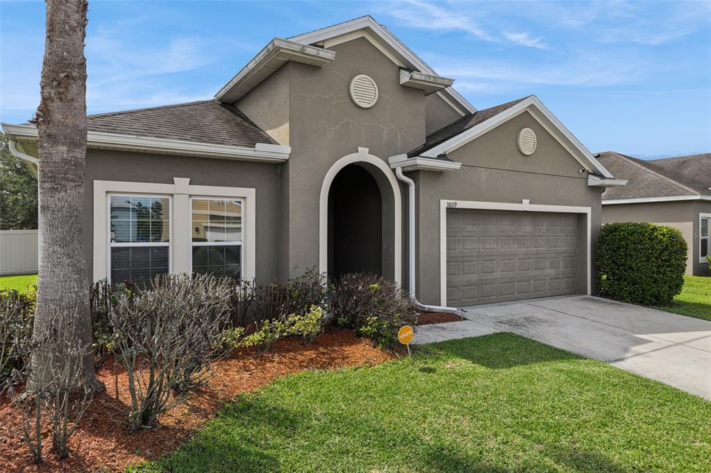 A single-story house with a gray stucco exterior, a two-car garage, and a front entryway — 3809 ENCHANTMENT LANE, ST CLOUD, FL