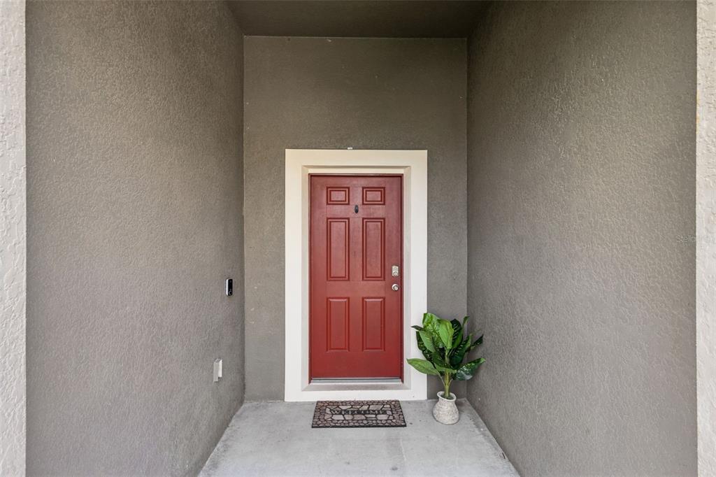 A red front door with white trim is set within a recessed concrete entryway — 3809 ENCHANTMENT LANE, ST CLOUD, FL