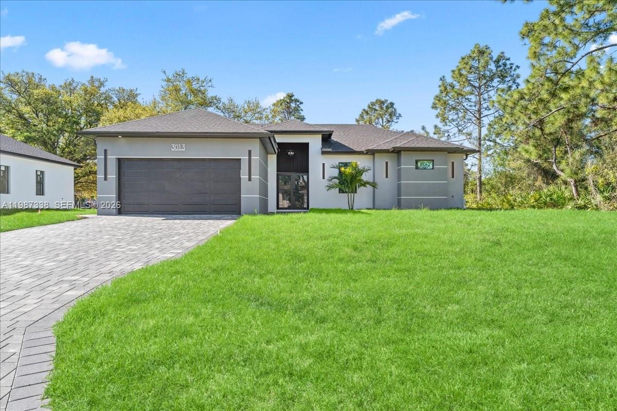 A modern single-story house with a gray garage, white stucco walls, and a paved driveway — 3013 14th St W,, Lehigh Acres FL 33971, LEHIGH ACRES, FL