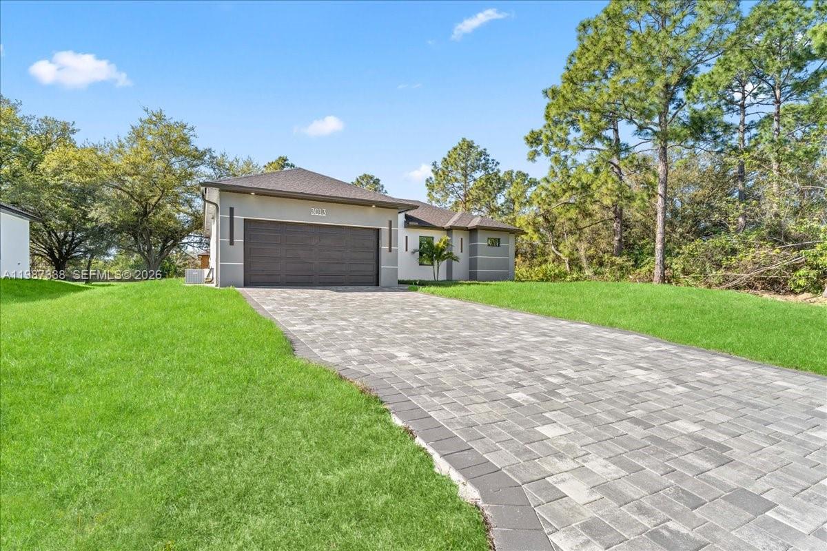 A single-story house with a paved driveway and a two-car garage under a blue sky — 3013 14th St W,, Lehigh Acres FL 33971, LEHIGH ACRES, FL