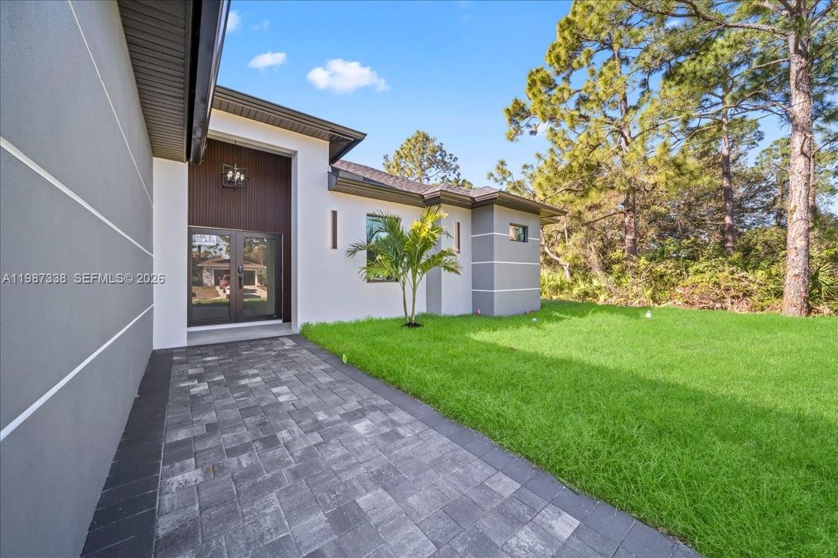 A paved walkway leads to the dark-framed glass front door of a modern house — 3013 14th St W,, Lehigh Acres FL 33971, LEHIGH ACRES, FL