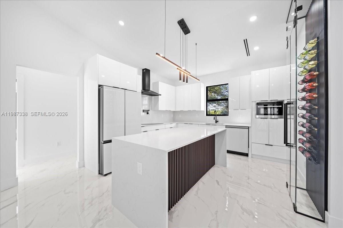 A modern white kitchen features a marble-topped island, high-gloss cabinetry, and a glass wine rack — 3013 14th St W,, Lehigh Acres FL 33971, LEHIGH ACRES, FL