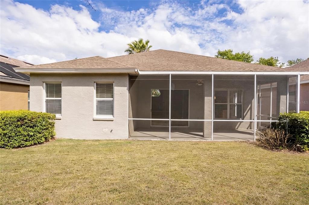 The rear exterior of a single-story house features a screened-in patio and a grassy yard — 985 RIDGEMOUNT PLACE, LAKE MARY, FL