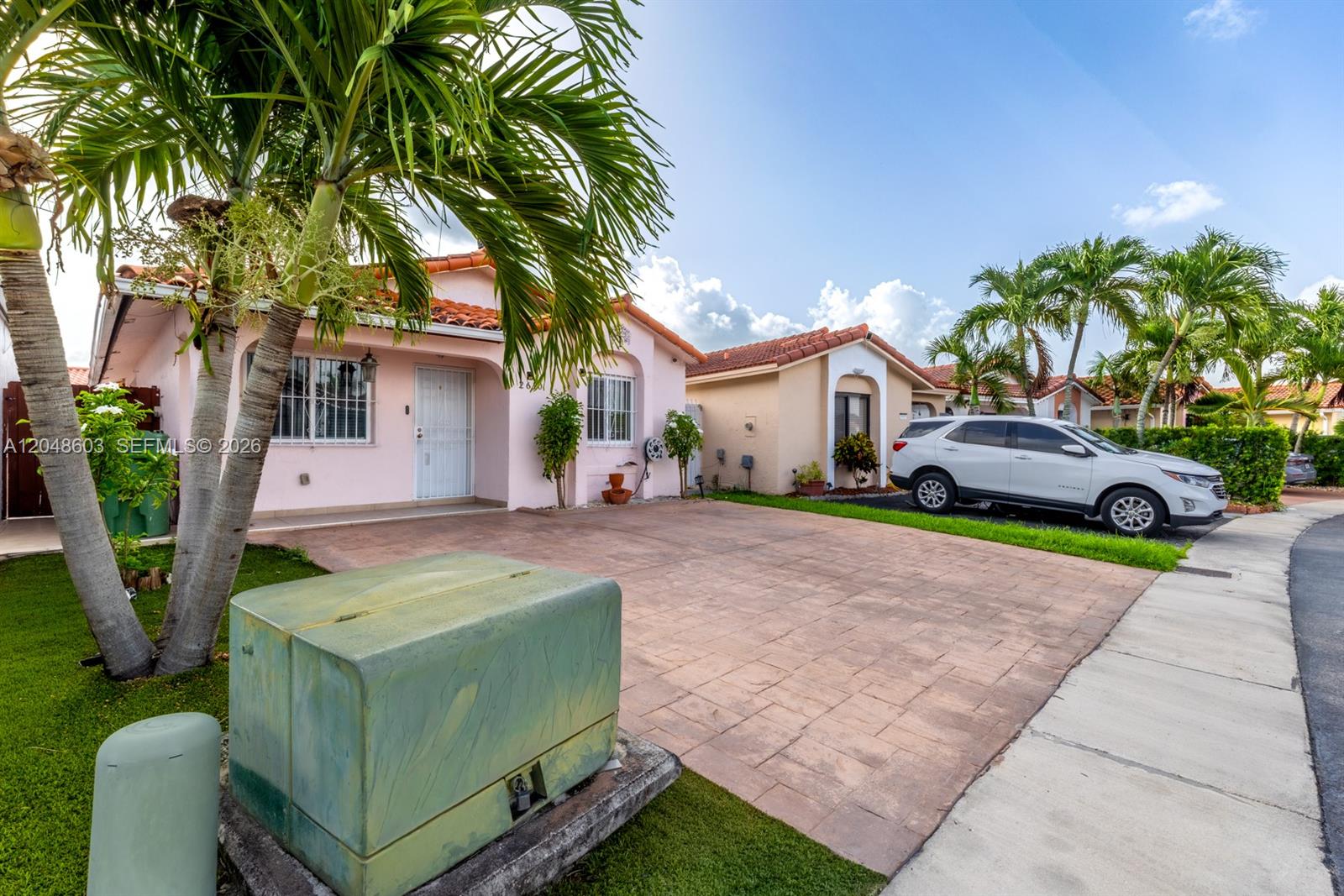 A pink house with a paved driveway and palm trees sits next to a white SUV — 2610 W 65th St # 2610, Hialeah FL 33016, HIALEAH, FL