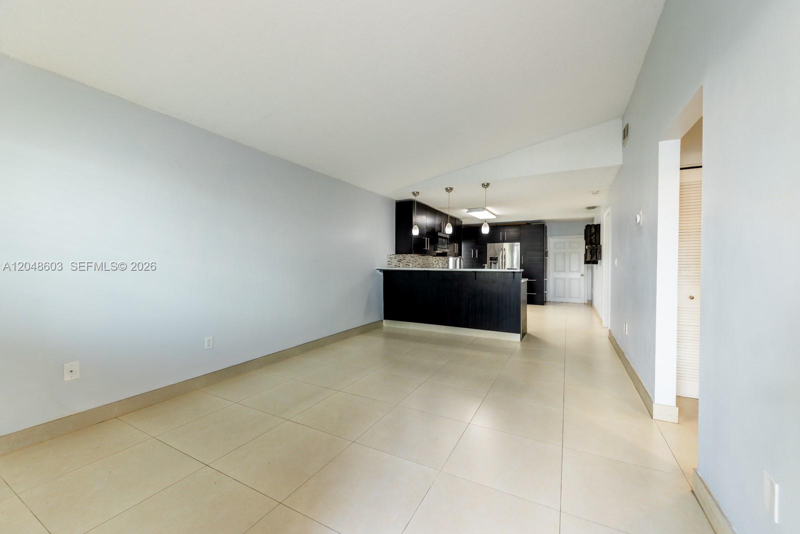 An open-concept kitchen with dark cabinetry and a breakfast bar overlooks a tiled living area — 2610 W 65th St # 2610, Hialeah FL 33016, HIALEAH, FL