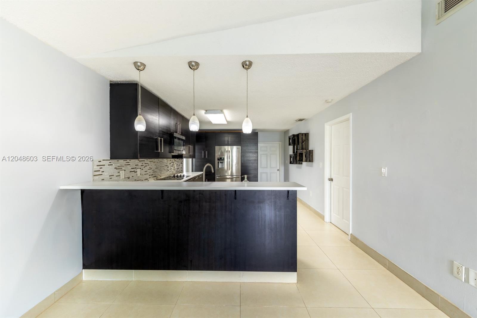 A kitchen features dark wood cabinetry, a breakfast bar, and light-colored tile flooring — 2610 W 65th St # 2610, Hialeah FL 33016, HIALEAH, FL
