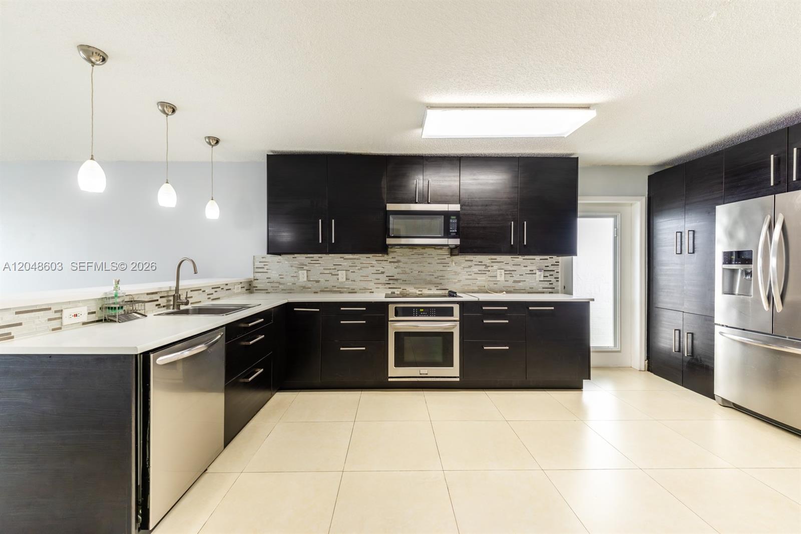 A kitchen features dark wood cabinets, stainless steel appliances, and light-colored tile flooring — 2610 W 65th St # 2610, Hialeah FL 33016, HIALEAH, FL