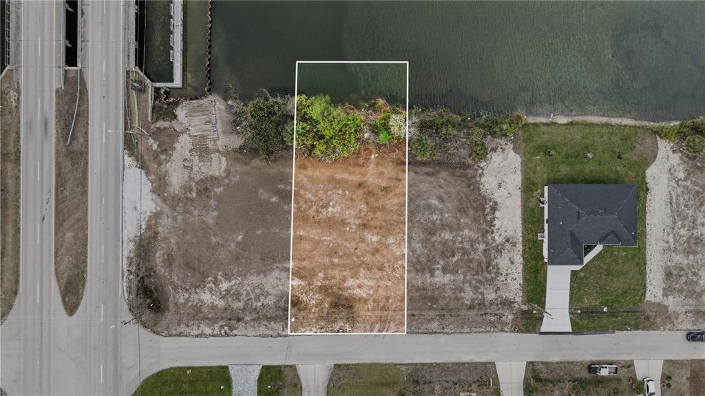 An aerial view shows a vacant rectangular waterfront lot outlined in white near a bridge — 1525 NW 17TH STREET, CAPE CORAL, FL
