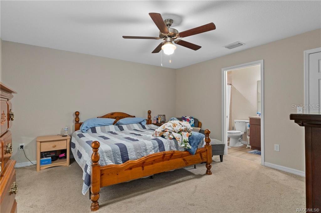 A bedroom with a wooden bed frame, ceiling fan, and an attached bathroom — 3551 W BURGANDY DRIVE, CITRUS SPRINGS, FL