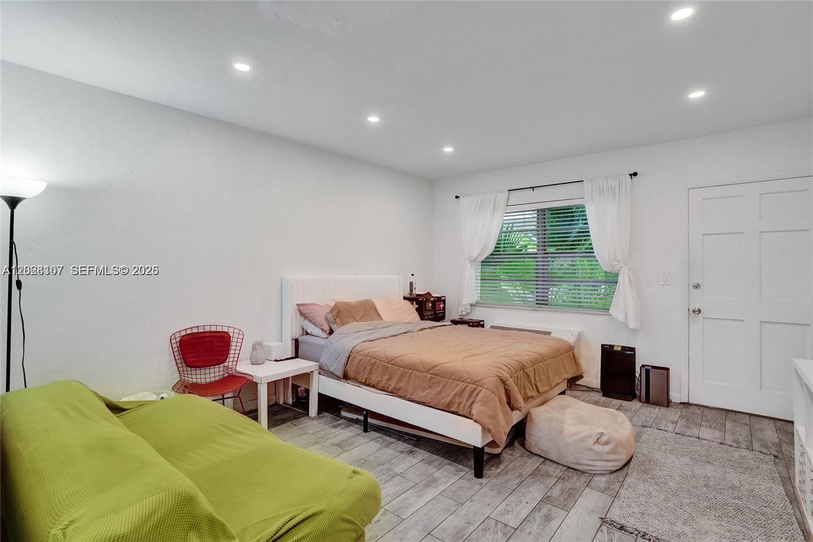 A bedroom features a bed, a green sofa, a red chair, and wood-look tile flooring — 911 Meridian Ave # 104, Miami Beach FL 33139, MIAMI BEACH, FL