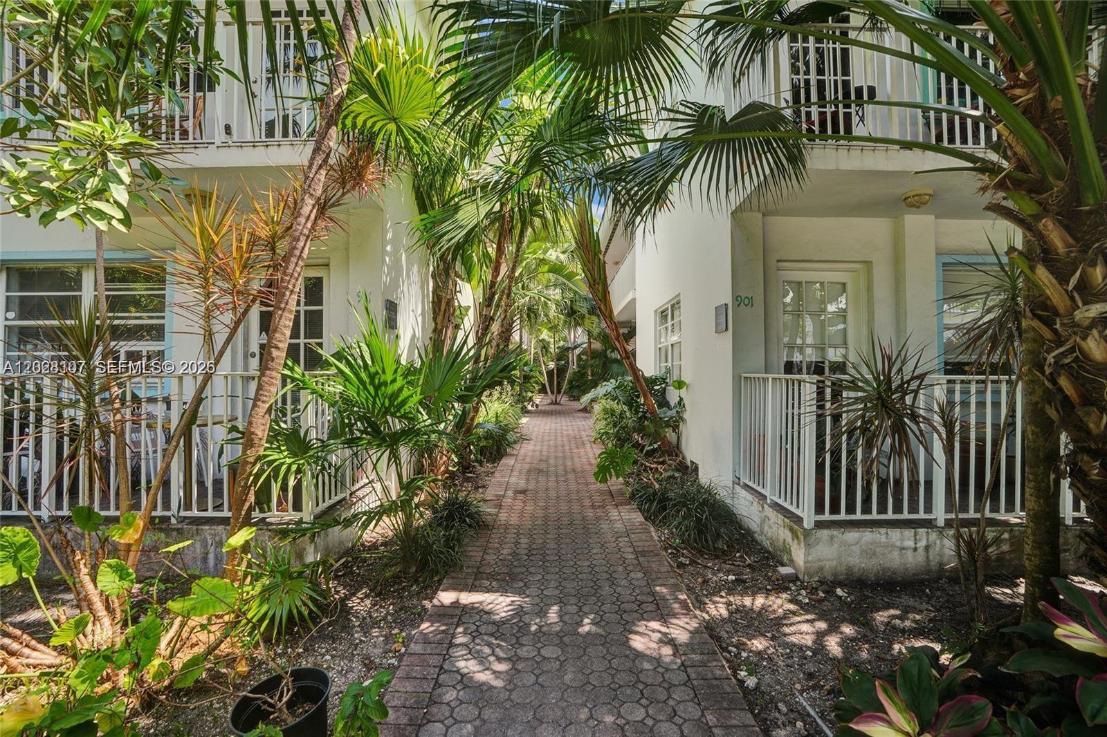 A brick walkway leads between two white multi-story buildings surrounded by lush tropical landscaping — 911 Meridian Ave # 104, Miami Beach FL 33139, MIAMI BEACH, FL
