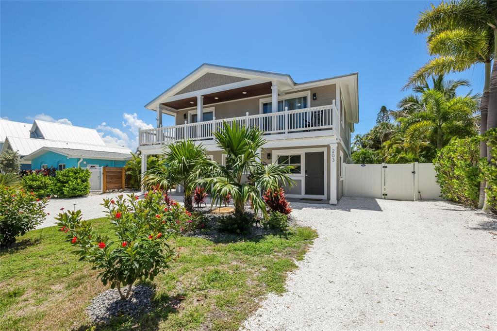 A two-story house with a white balcony and gravel driveway sits under a clear sky — 203 72ND STREET, HOLMES BEACH, FL