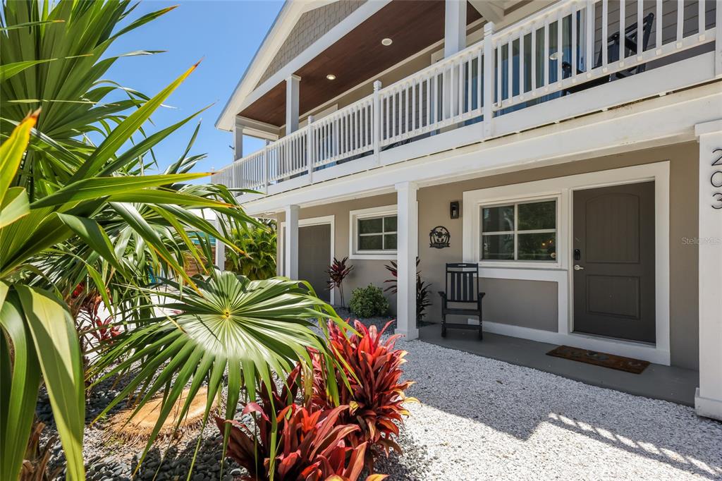 The exterior of a two-story building features a white porch, gray door, and landscaping — 203 72ND STREET, HOLMES BEACH, FL