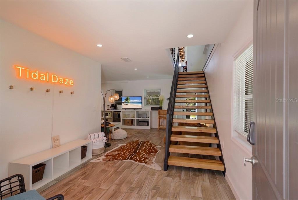 An interior view shows a living area with wood-look flooring, a staircase, and neon signage — 203 72ND STREET, HOLMES BEACH, FL