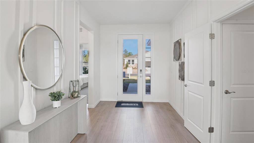 A bright entryway features light wood flooring, white board-and-batten walls, and a round wall mirror — 7052 SW 44TH CIRCLE, OCALA, FL