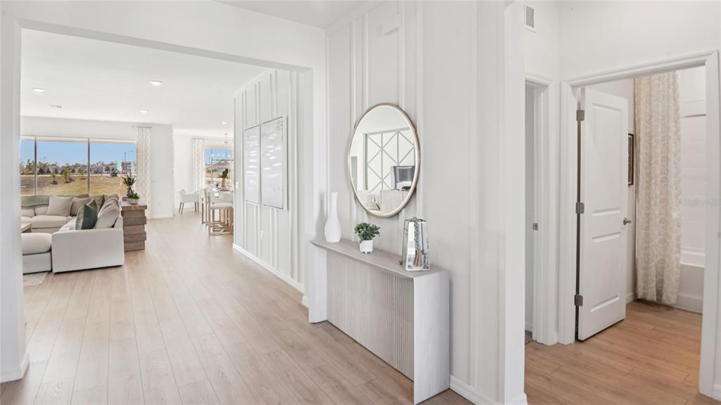 A bright entryway features a console table, round mirror, and wood-look flooring leading to living areas — 7052 SW 44TH CIRCLE, OCALA, FL
