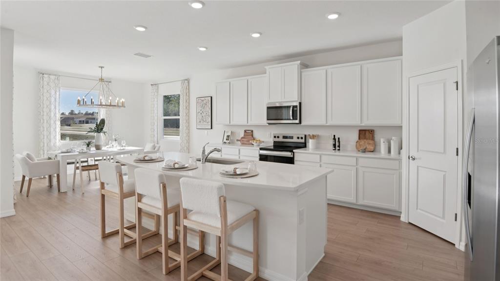A bright kitchen features white cabinets, a central island with bar seating, and dining area — 7052 SW 44TH CIRCLE, OCALA, FL