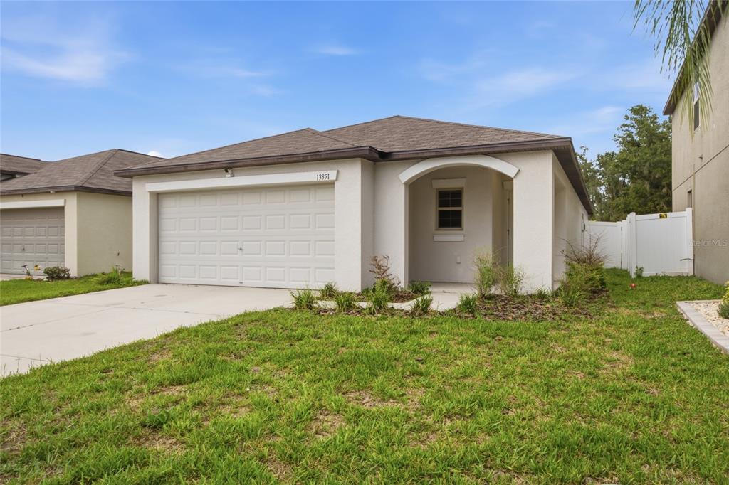 A single-story house with a beige stucco exterior, a two-car garage, and a covered entryway — 13351 WILLOW BLUESTAR LOOP, RIVERVIEW, FL